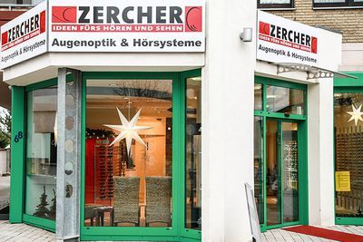 Eingang eines Augenoptik- und Hörsysteme-Fachgeschäfts mit grüner Glasfront und Stern-Dekoration.